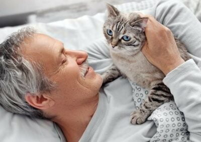 An elderly man with his furry feline friend sitting on his lap.